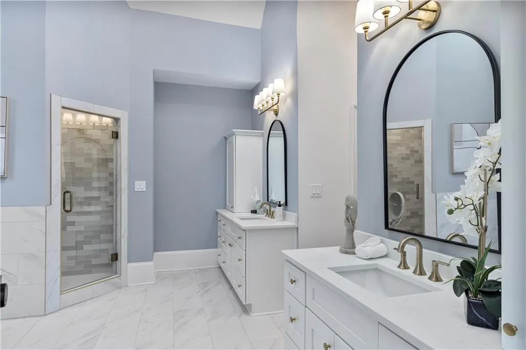 Full bath with two vanities, a shower stall, and light marble finish flooring