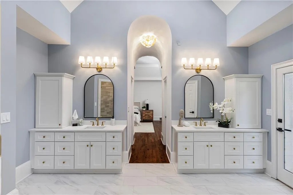 Ensuite bathroom with two vanities, light marble finish flooring, and lofted ceiling