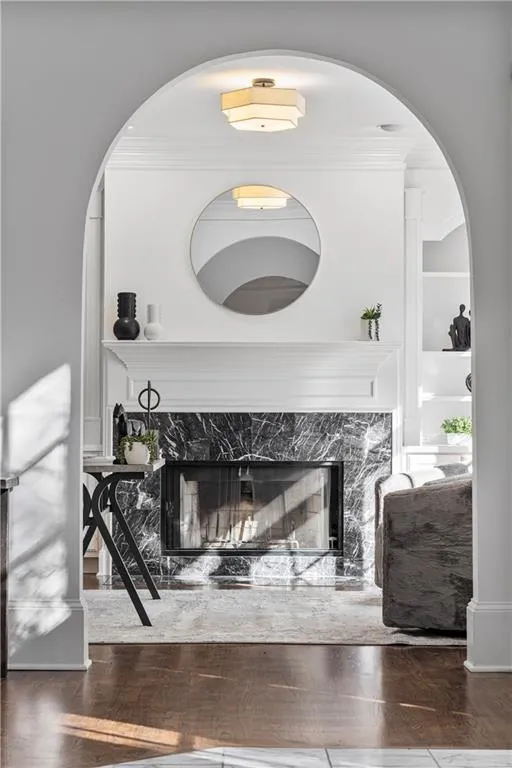 Living area with crown molding, built in shelves, a high end fireplace, arched walkways, and wood finished floors