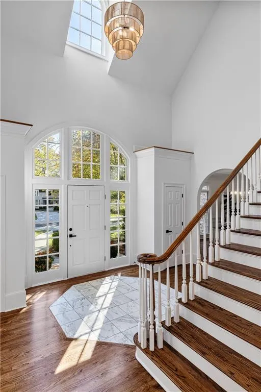 Entryway featuring a high ceiling, wood finished floors, a chandelier, stairs, and arched walkways