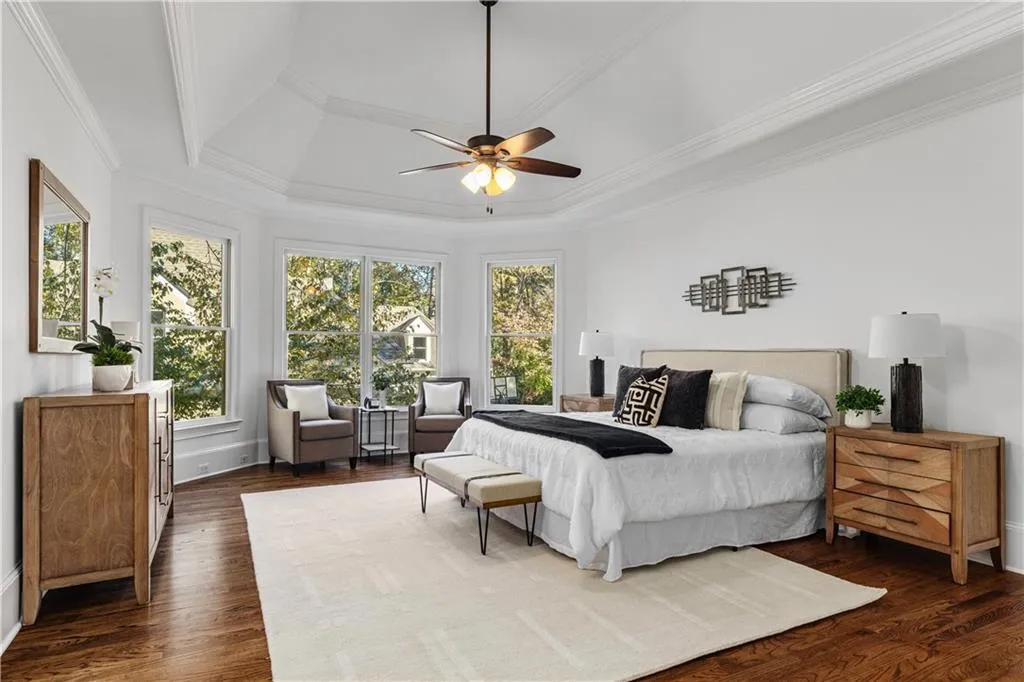 Bedroom with a raised ceiling, ornamental molding, multiple windows, and dark wood-style floors
