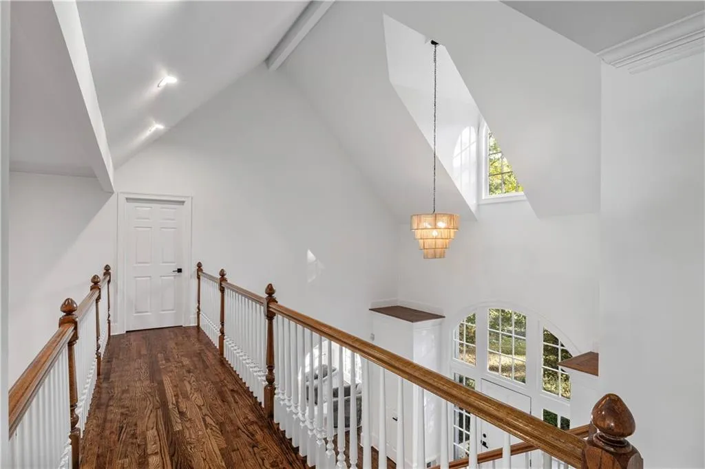 Corridor with high vaulted ceiling, beamed ceiling, healthy amount of natural light, dark wood finished floors, and a chandelier