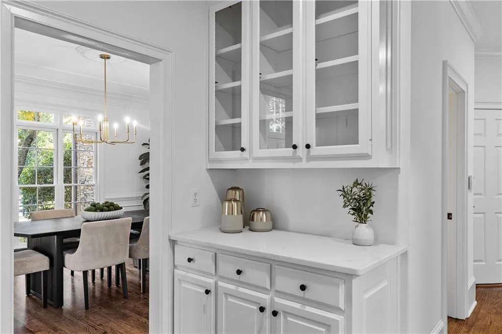 Bar with dark wood-style flooring, glass insert cabinets, light stone countertops, white cabinetry, and crown molding