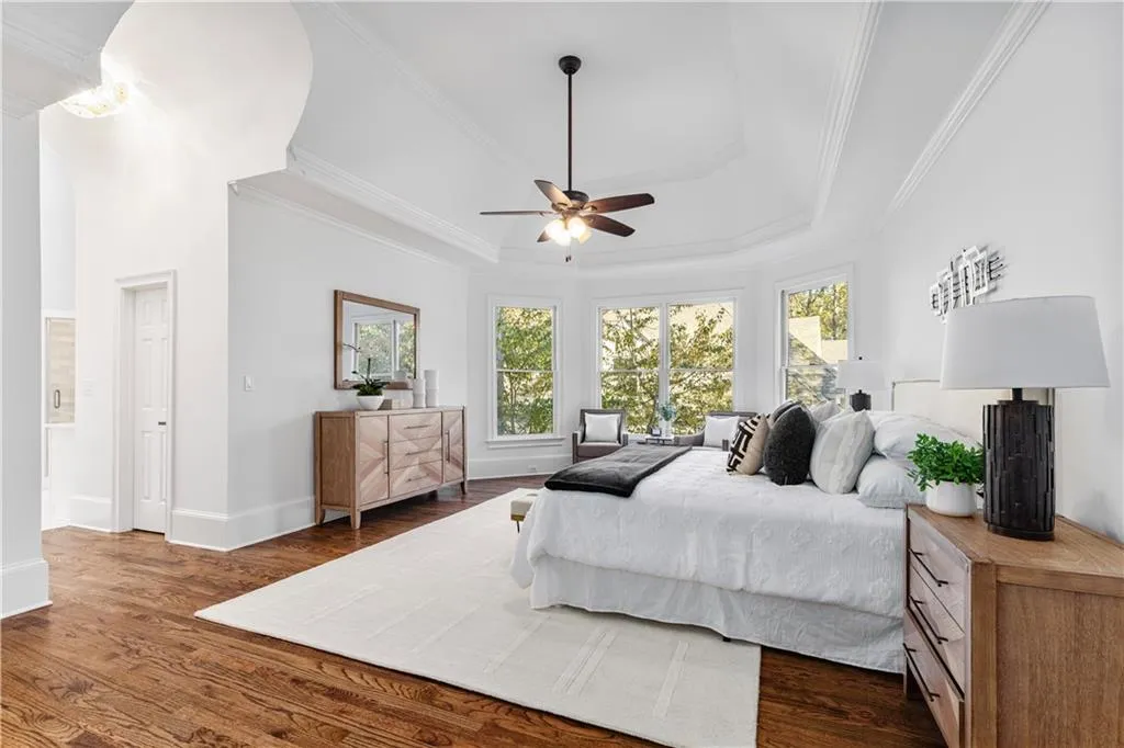 Bedroom with crown molding, a tray ceiling, dark wood-type flooring, and a ceiling fan