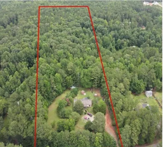 Extensive wooded lot featuring a single-story dwelling, surrounding mature trees, and a visible boundary line