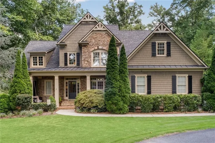 Craftsman-style exterior featuring stone and shake siding, multiple gables, a covered front porch with columns, and dark window shutters