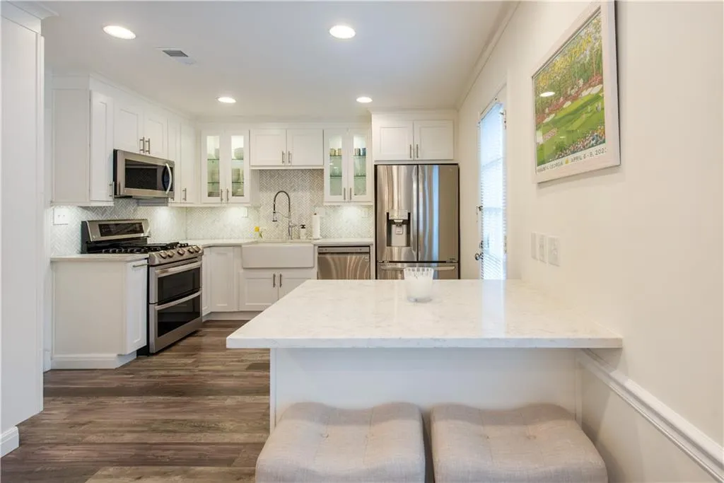 Kitchen with stainless steel appliances, glass insert cabinets, a peninsula, dark wood-type flooring, and tasteful backsplash