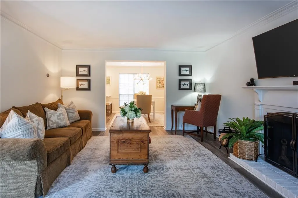 Living room with ornamental molding, wood finished floors, a chandelier, and a brick fireplace