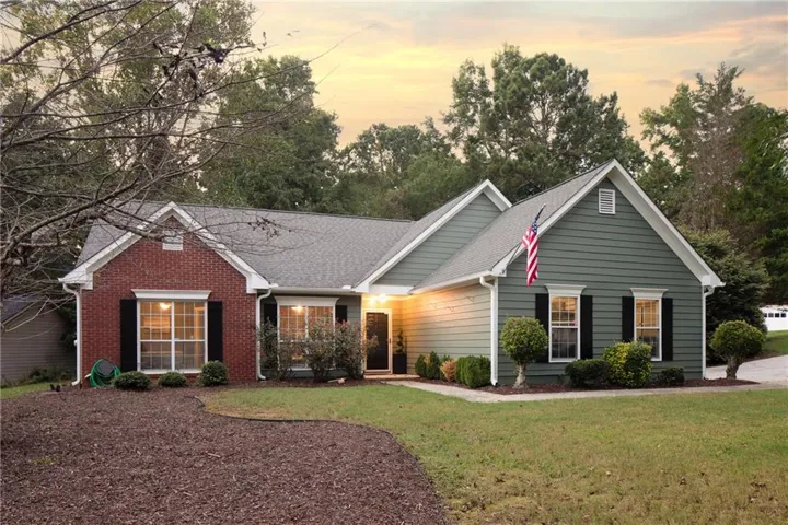 Exterior featuring brick and siding finishes, a gabled roofline, black louvered shutters, and a manicured lawn with landscape beds