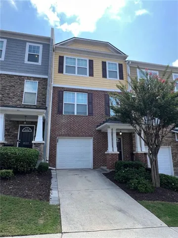Three-story townhome featuring a brick facade on the lower level and yellow siding on the upper two levels