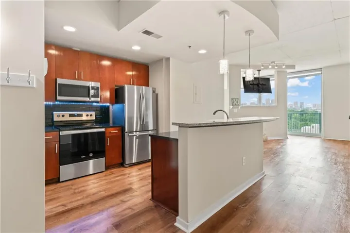 Open-concept kitchen featuring stainless steel appliances, wood-finish flooring, a kitchen island with a stone-finish countertop, and recessed lighting
