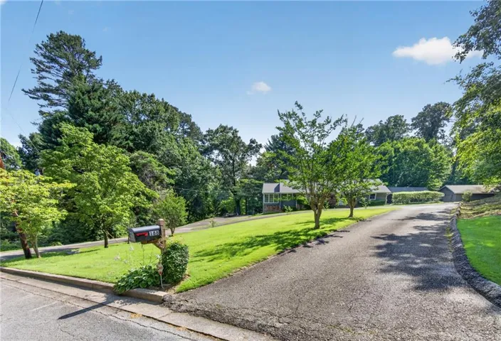 Paved driveway extending to the property, bordered by a manicured lawn and mature trees