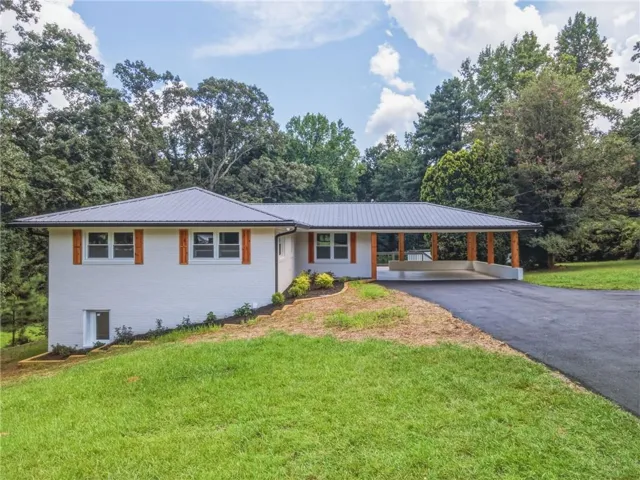 White brick exterior featuring a gray metal roof, wood-finish shutters, and a covered carport with wood-finish support columns