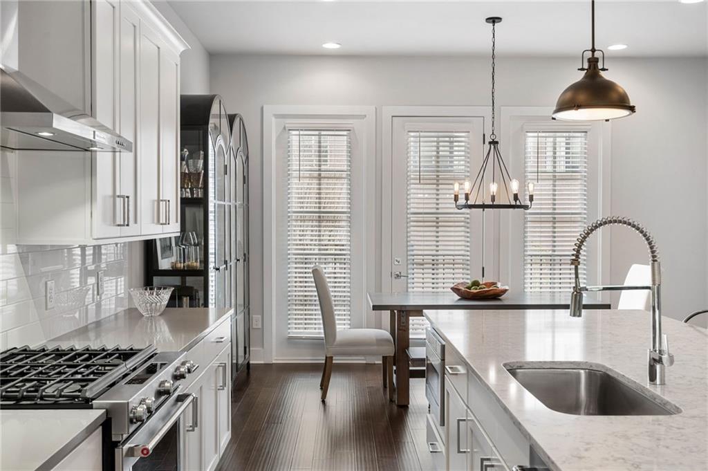 Kitchen with hanging light fixtures, high end range, wall chimney exhaust hood, dark wood-type flooring, and backsplash