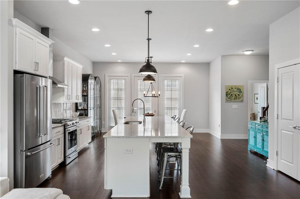Kitchen with sink, a center island with sink, hanging light fixtures, appliances with stainless steel finishes, and white cabinets