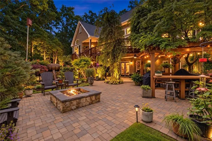 Expansive paver patio featuring a stone fire pit, wood pergola, and integrated outdoor lighting