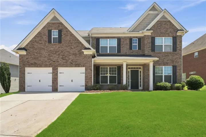 Brick-front residence featuring a two-car garage, manicured lawn, and a covered portico entrance with white columns