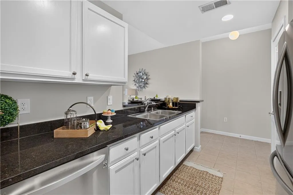 Kitchen featuring white cabinetry with dark hardware, dark countertops, a double basin sink, and stainless steel dishwasher