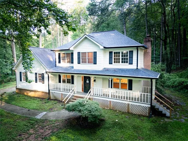 Two-story traditional residence featuring white siding, a dark roof, and a covered front porch with white railings