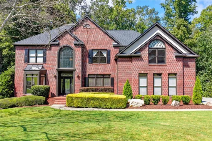 Brick exterior with multiple gables, arched entry, bay window, and a landscaped front yard