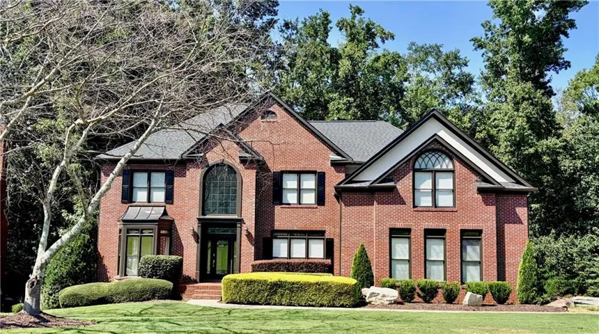 Brick exterior with multiple gables, arched windows, dark shutters, and a well-maintained front lawn