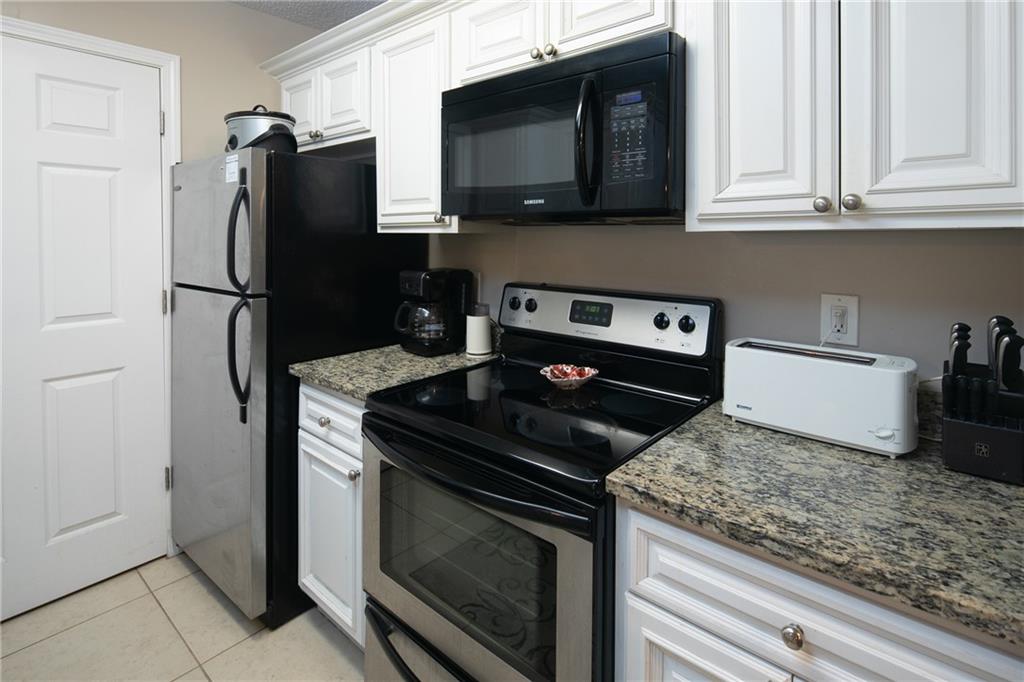 Kitchen featuring appliances with stainless steel finishes, light tile floors, dark stone counters, and white cabinets
