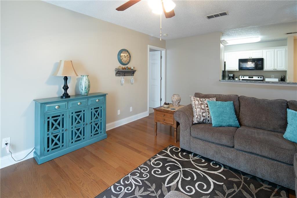Living room featuring ceiling fan, a textured ceiling, and light wood-type flooring