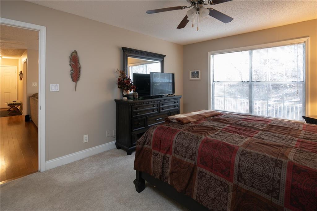Bedroom with ceiling fan, light colored carpet, and a textured ceiling