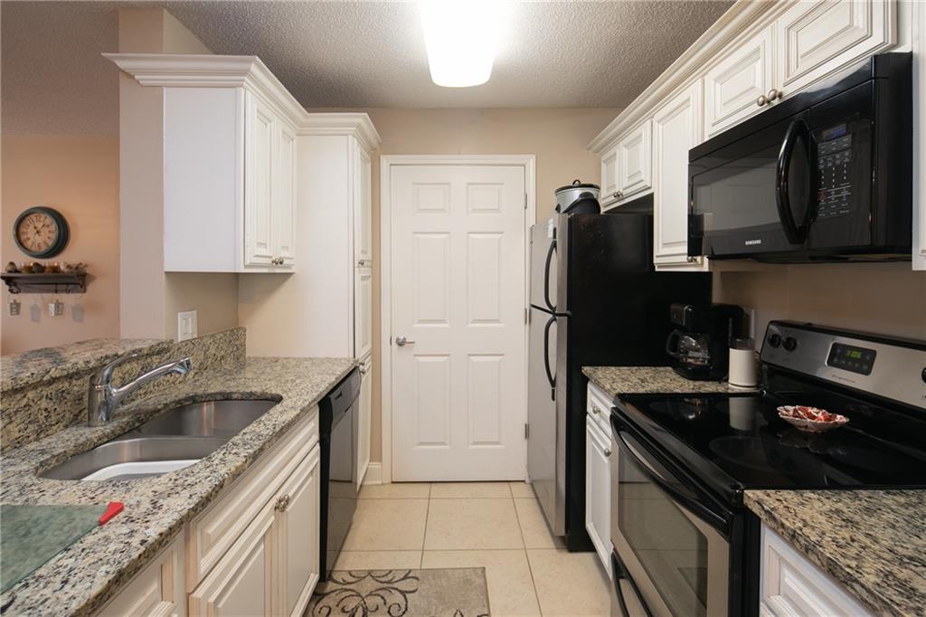 Kitchen with light tile flooring, sink, black appliances, and white cabinetry