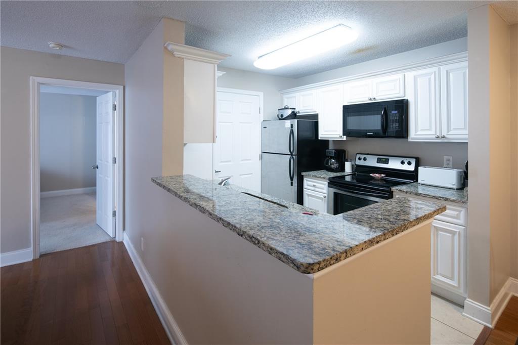 Kitchen with white cabinets, kitchen peninsula, appliances with stainless steel finishes, and light wood-type flooring