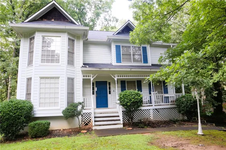 White clapboard exterior featuring a prominent bay window, a covered front porch with lattice detailing, a vibrant blue front door, and matching blue window shutters