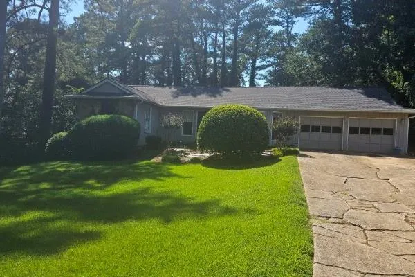 Ranch-style residence featuring a gray shingle roof, dual garage doors, and a concrete driveway