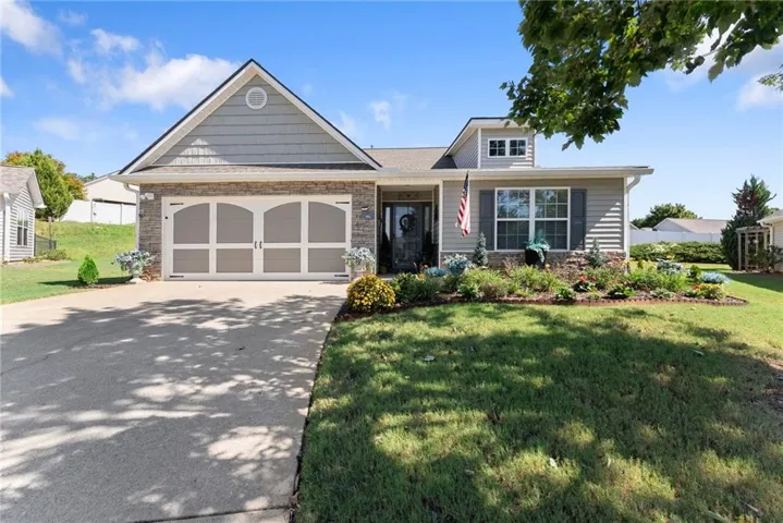 Exterior featuring stone veneer and horizontal siding, an arched double garage door, a prominent front gable, and a landscaped front garden