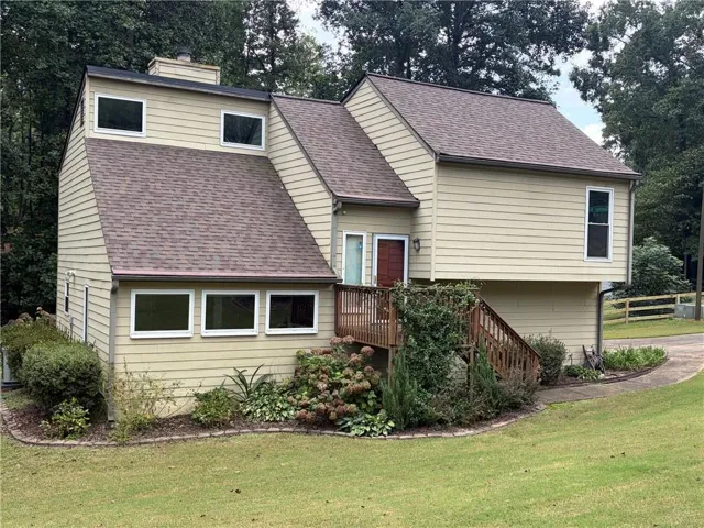 Multi-level exterior with light-colored siding, a brown shingle roof, and a prominent front deck with wooden stairs