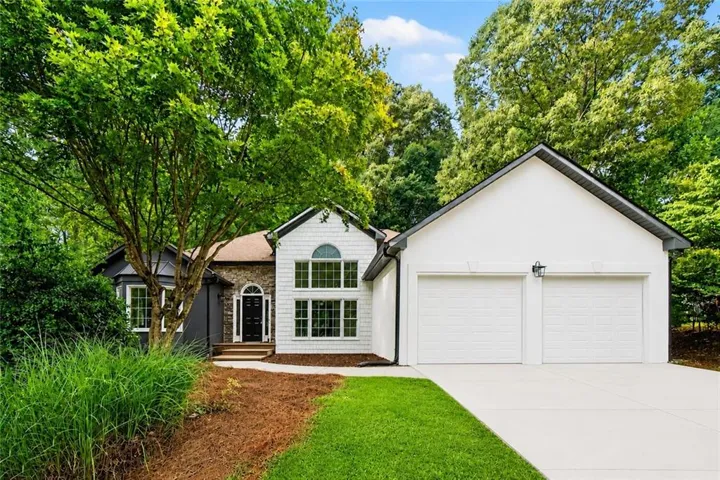 Contemporary façade featuring white siding, dark gray accents, a prominent two-car garage, and a peaked roofline