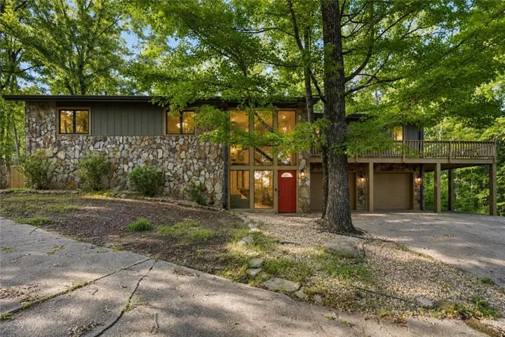 Mid-century modern residence featuring extensive stone veneer, a striking red front door, expansive windows, a multi-level deck, and two garage doors