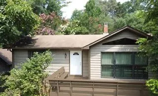 Exterior featuring horizontal siding, an arched entry door, a large fixed window, a brick chimney, and a wooden deck with a built-in bench