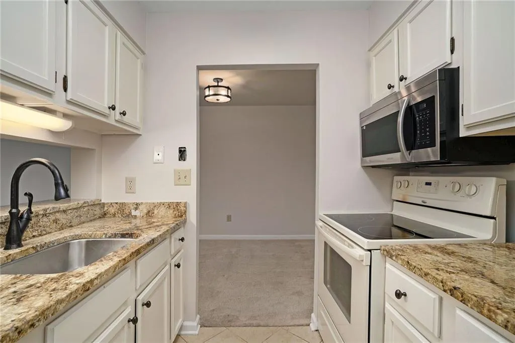 Kitchen featuring sink, electric stove, white cabinets, light colored carpet, and light stone countertops