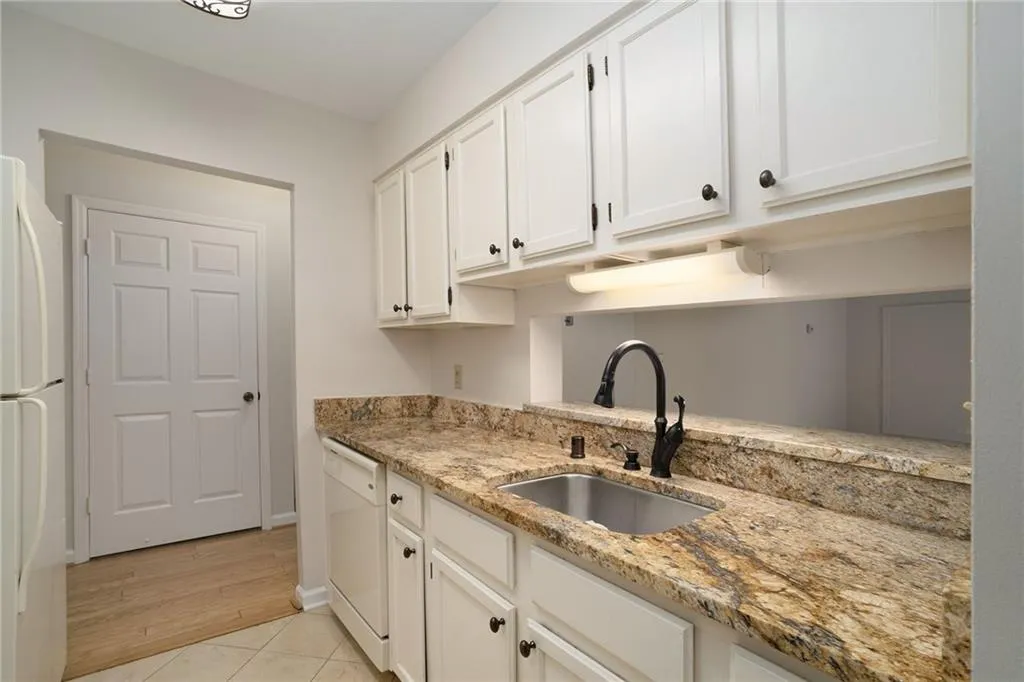 Kitchen featuring white appliances, sink, light tile floors, light stone counters, and white cabinets