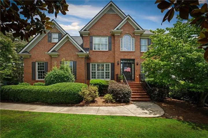 Brick facade residence featuring a front entry staircase, arched window detail, dark shutters, and established landscaping