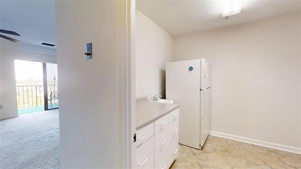 Kitchen with freestanding refrigerator, light countertops, white cabinets, and ceiling fan