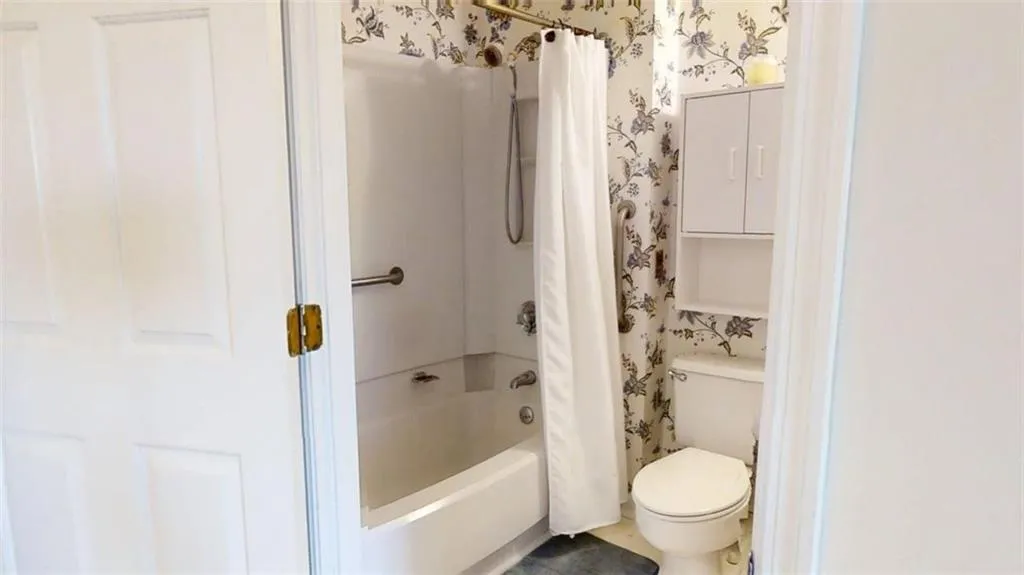 Full bathroom featuring shower / tub combo with curtain and wallpapered walls