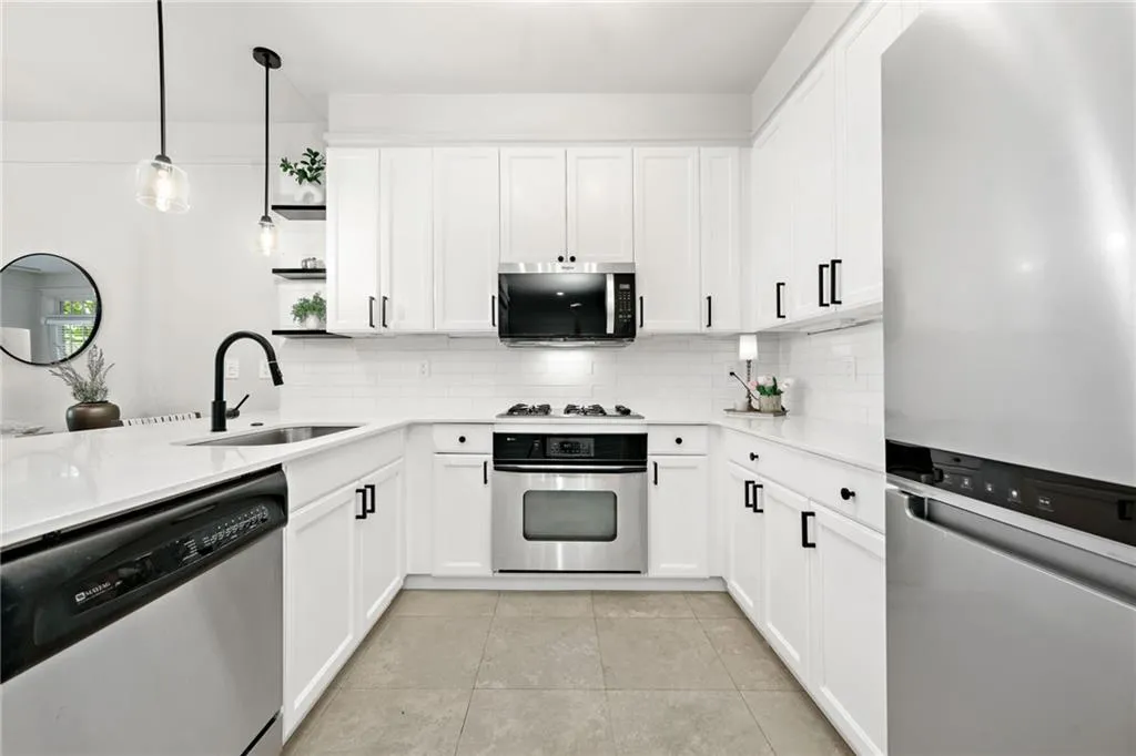 Kitchen with stainless steel appliances, a sink, decorative backsplash, and white cabinetry