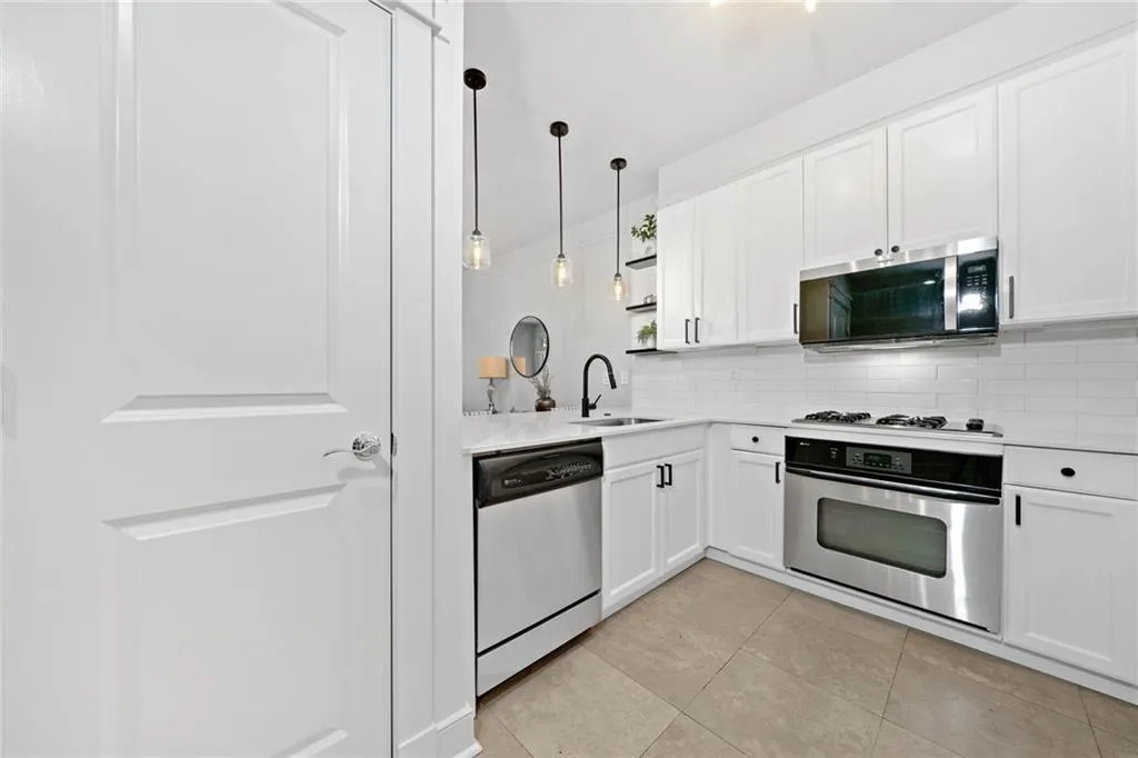 Kitchen with stainless steel appliances, a sink, tasteful backsplash, light countertops, and white cabinets