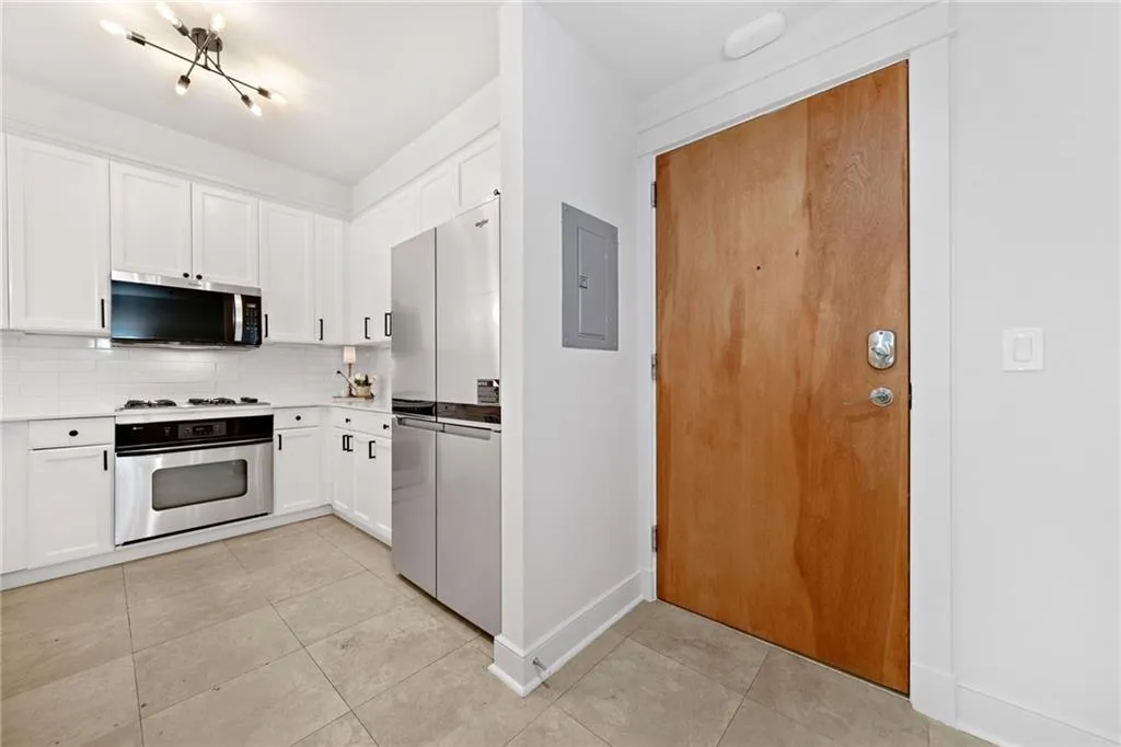 Kitchen featuring appliances with stainless steel finishes, decorative backsplash, light countertops, white cabinetry, and light tile patterned flooring