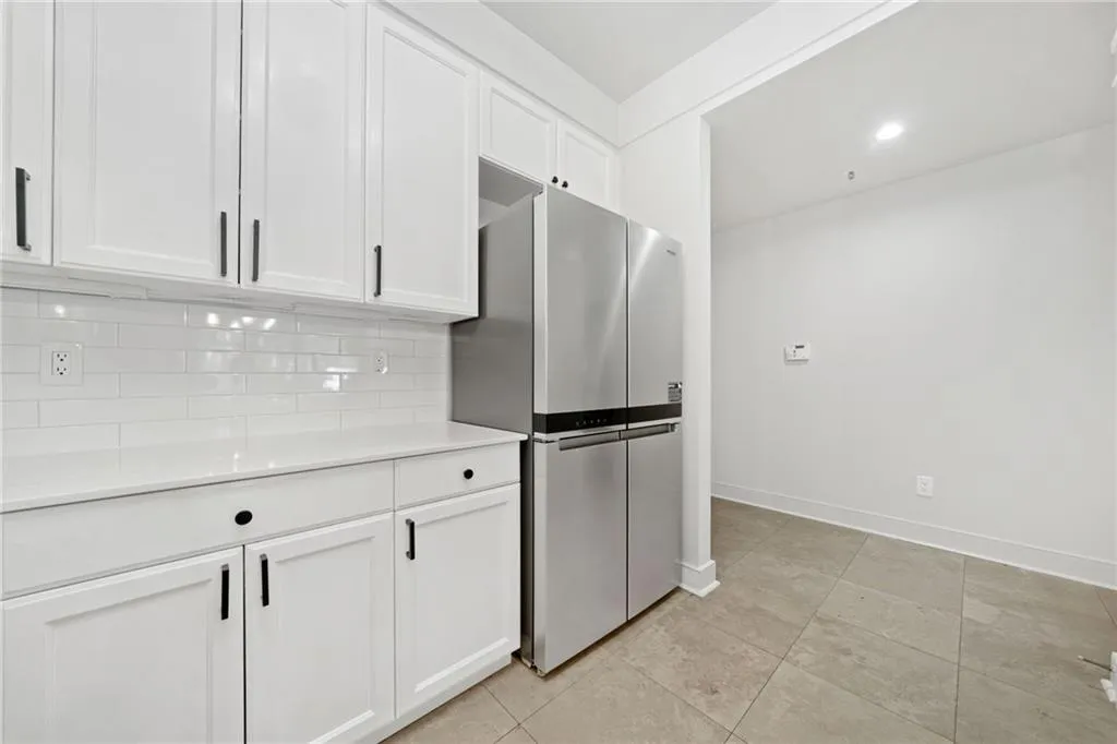 Kitchen featuring freestanding refrigerator, backsplash, white cabinetry, light countertops, and baseboards