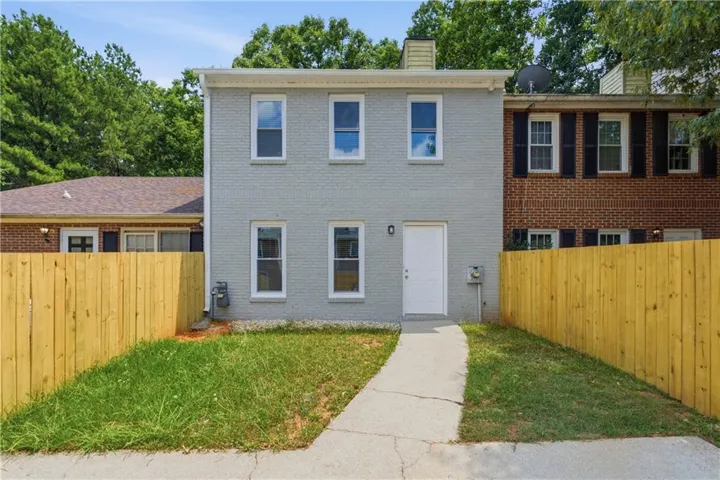 Two-story exterior with light gray painted brick, a crisp white entry door, and a concrete walkway