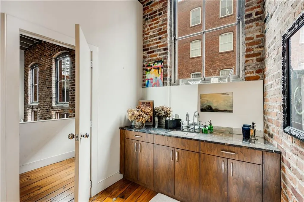 Bar featuring brick wall, light wood-type flooring, dark stone counters, and brown cabinets