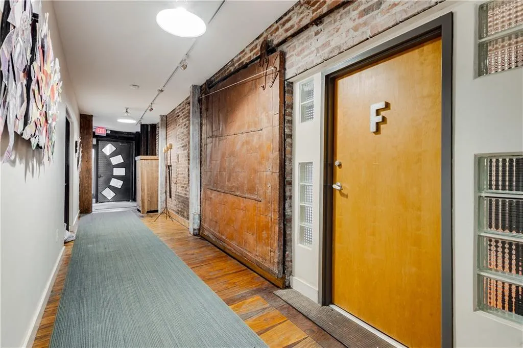 Hall with brick wall, wood finished floors, track lighting, and an accent wall