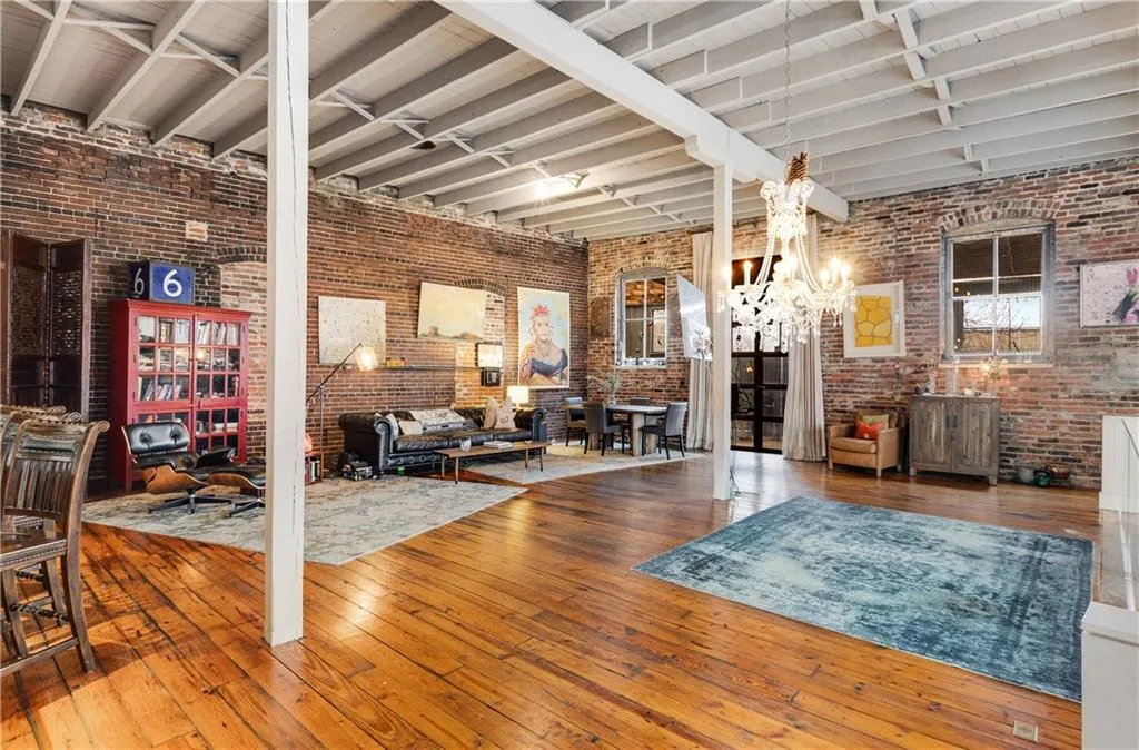 Living room with hardwood / wood-style flooring, brick wall, a chandelier, and beam ceiling